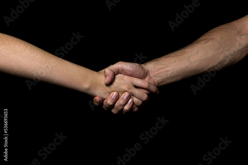 A man's hand squeezes a woman's hand on a black background. The concept of agreement and equality