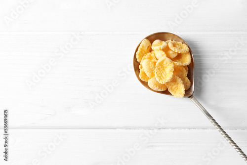 Metal spoon of tasty crispy corn flakes on white wooden table, top view. Space for text