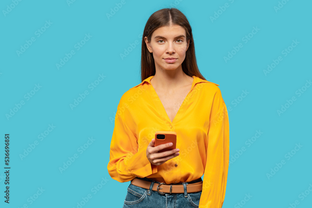 Serious irritated woman with indignant face after reading fake news using phone on blue background Serious irritated woman with indignant face after reading fake news using phone on blue background