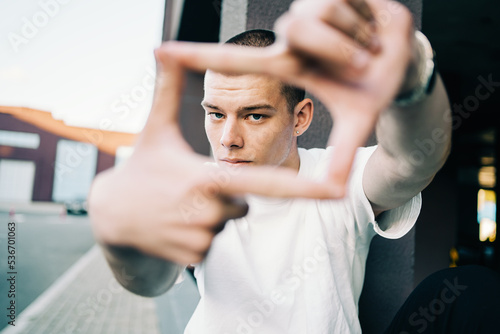 Bild auf Leinwand Handsome young man in early 20s looks into camera through a frame formed with his fingers