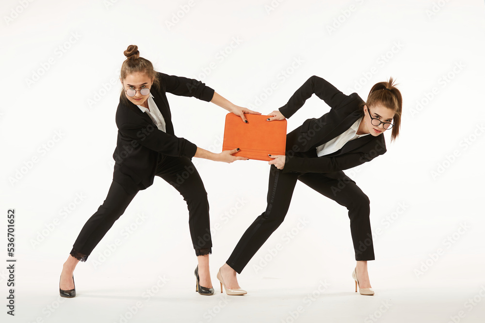 Obraz premium The competitive struggle of two girls in office clothes. Pure white background. The concept of business and corporate relationships in the enterprise.