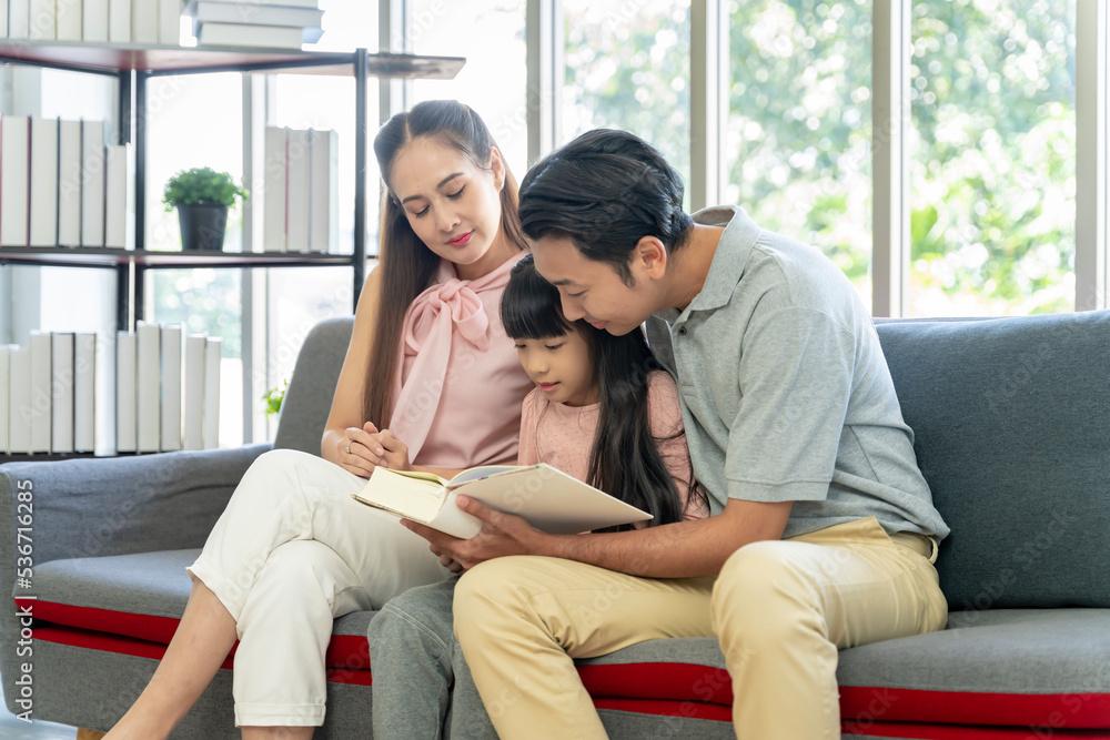 Asian family portrait Parents and daughters are happily reading together on the sofa in the house together. Asian family portrait Parents and daughters are happily reading together on the sofa in the house together.
