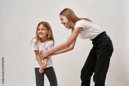 Teenage girl tickling her little sister on white