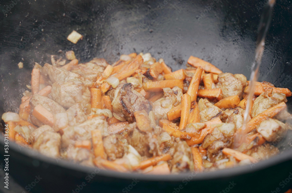 Water is poured into the cauldron where onions and meat and carrots are fried. Water is poured into the cauldron where onions and meat and carrots are fried.