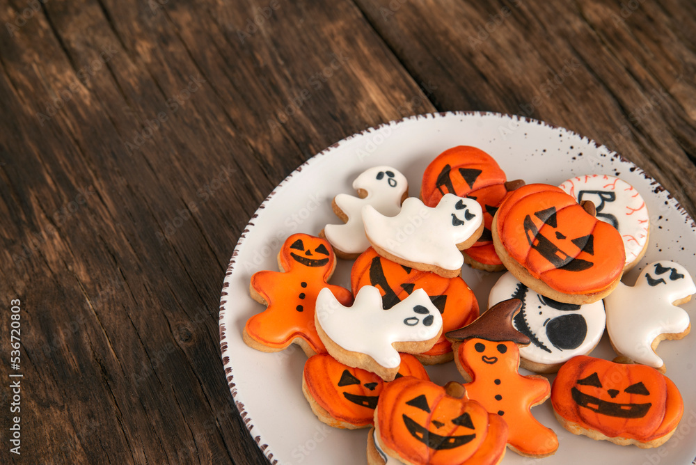 Orange Halloween cookies in the shape of pumpkin ghosts in big plate on a wooden table. Place for text. Top view