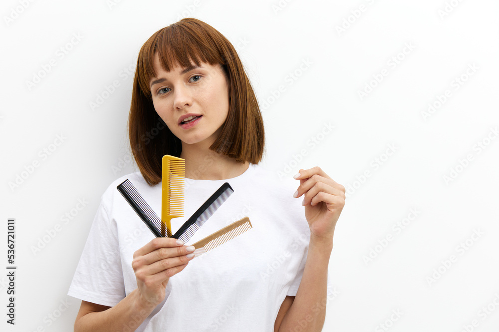 pleasant woman with a beautiful hairstyle holds out a lot of combs in her hand to the camera and looks through them, raising her hand in a relaxed gesture, standing on a white background in a T-shirt pleasant woman with a beautiful hairstyle holds out a lot of combs in her hand to the camera and looks through them, raising her hand in a relaxed gesture, standing on a white background in a T-shirt