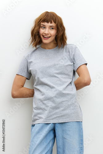 a vertical photo of a funny, joyful, sweet woman standing leaning on a white wall with a funny, emotional face.