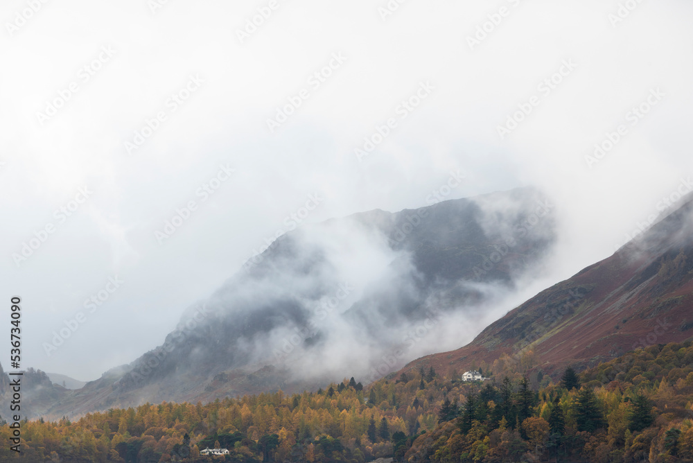Stunning landscape image of Catbells viewed acros Derwentwater during Autumn in Lake District with mist rolling across the hills and woodland