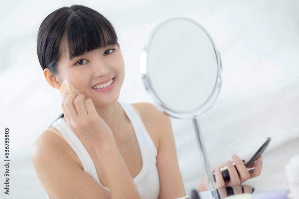Beautiful young asian woman applying powder puff on cheek makeup of cosmetic looking mirror, beauty of girl with skin face and wrinkle in the bedroom, cosmetology for female, skincare concept. Beautiful young asian woman applying powder puff on cheek makeup of cosmetic looking mirror, beauty of girl with skin face and wrinkle in the bedroom, cosmetology for female, skincare concept.