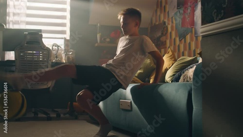 A teenager boy plays football while sitting on the bed alone in his room. Balancing the ball on his finger. Performing tricks. Sports, hobbies concept.