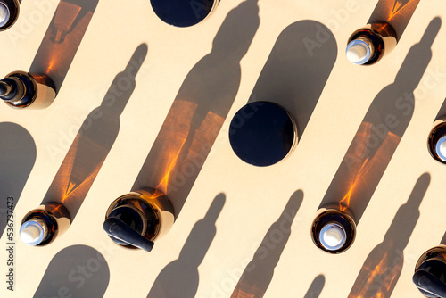 Pattern made with brown glass bottle of cosmetic products and strong shadow on beige background, as a backdrop or texture. Creative layout for your design