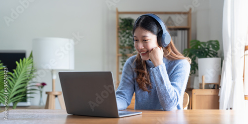 Young asian woman talk on video call at the table using headphones. Online remote work or learning concept