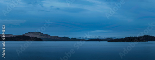 Beautiful landscape image of Loch Lomond and snowcapped mountain range in distance viewed from small village of Luss