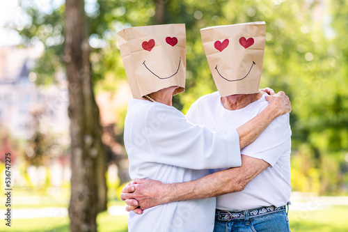 Senior couple in love dating outdoors - Creative portrait of couple of lovers with heart shaped drawing on papaer bags over the heads