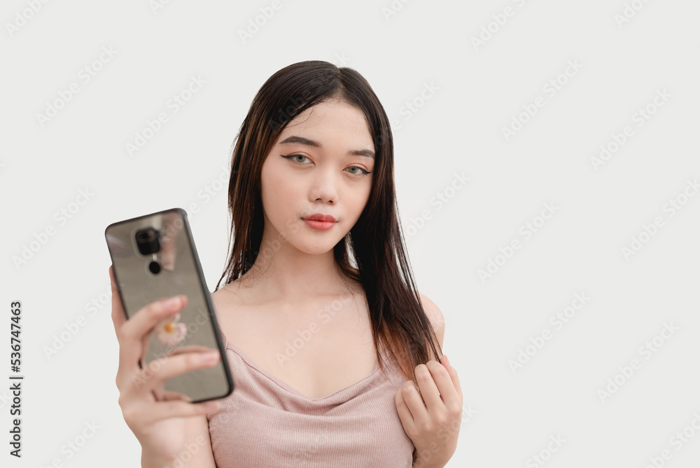 A lovely Asian girl poses for the camera while holding her phone to take a selfie. A lovely Asian girl poses for the camera while holding her phone to take a selfie.