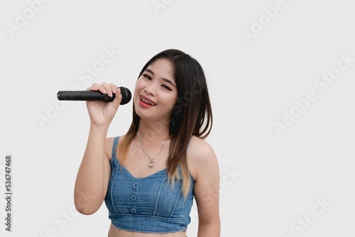A happy Southeast Asian woman smiles for the camera holding a wireless microphone as she shows her talent in singing. Studio shot isolated on white background.