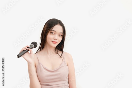 A young Asian female holds a wireless microphone while smiling for a studio shot isolated on white background.