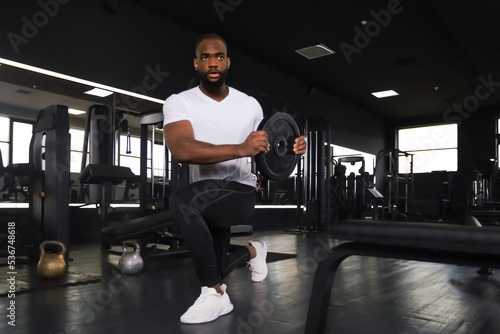 Handsome african man is working out with dumbbells at gym.