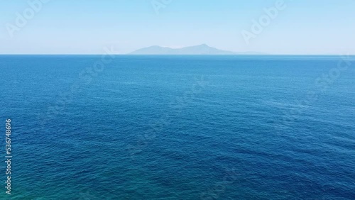 Aerial drone rising over vast blue ocean and rugged, remote tropical Atauro Island in the distance as seen from capital Dili, Timor Leste, Southeast Asia photo