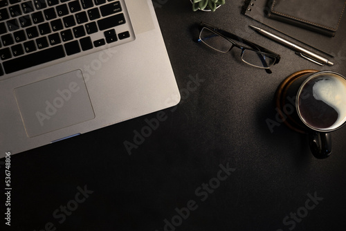 Laptop, eyeglasses, notepad and coffee cup on black leather background. Modern workplace.