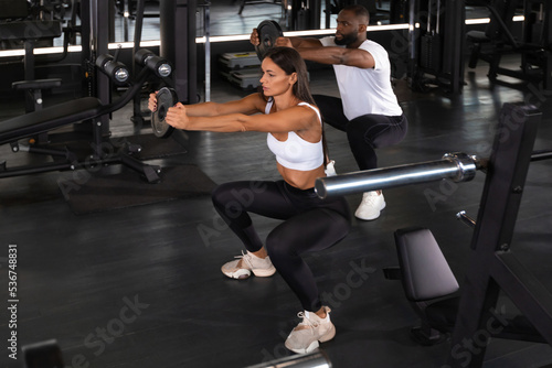 Fitness couple in sportswear doing squat exercises at gym.