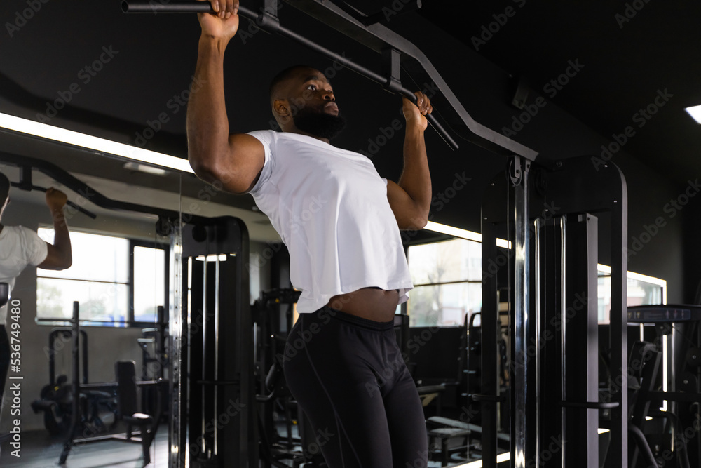 Fit and muscular african man pulling up on horizontal bar in a gym ...