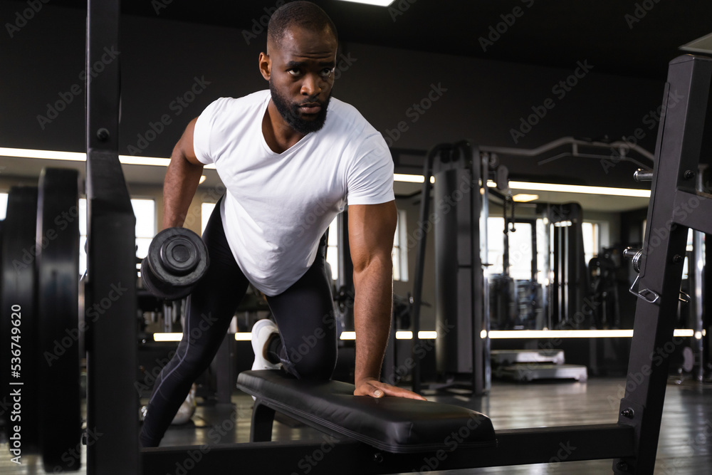 Naklejka premium Fit and muscular african man trains with dumbbells.