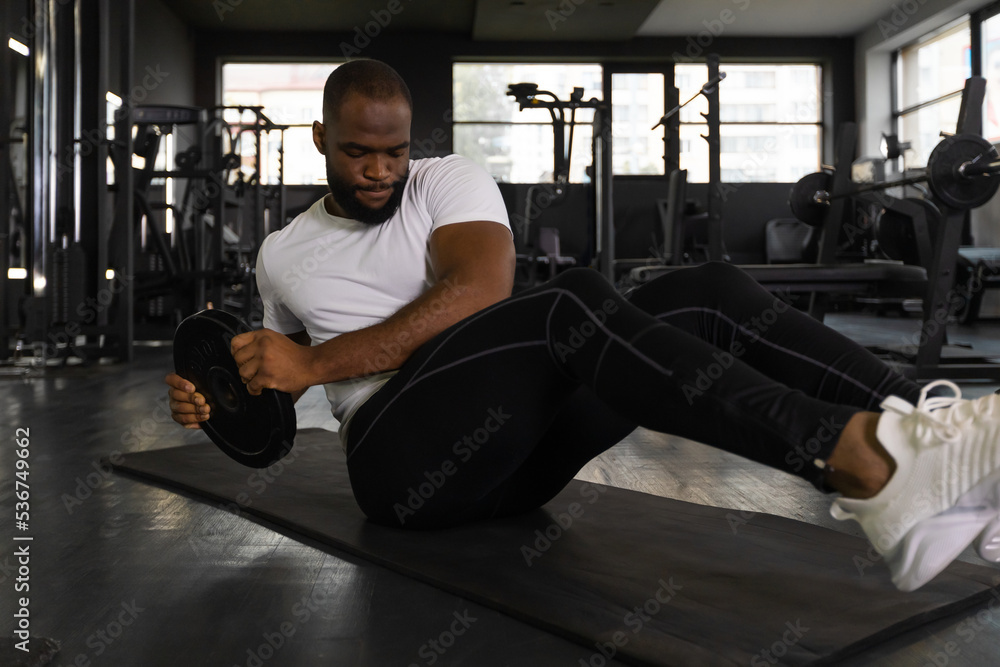 Handsome fit african man in sportwear doing crunches with damblebell in his hands at gym. Handsome fit african man in sportwear doing crunches with damblebell in his hands at gym.