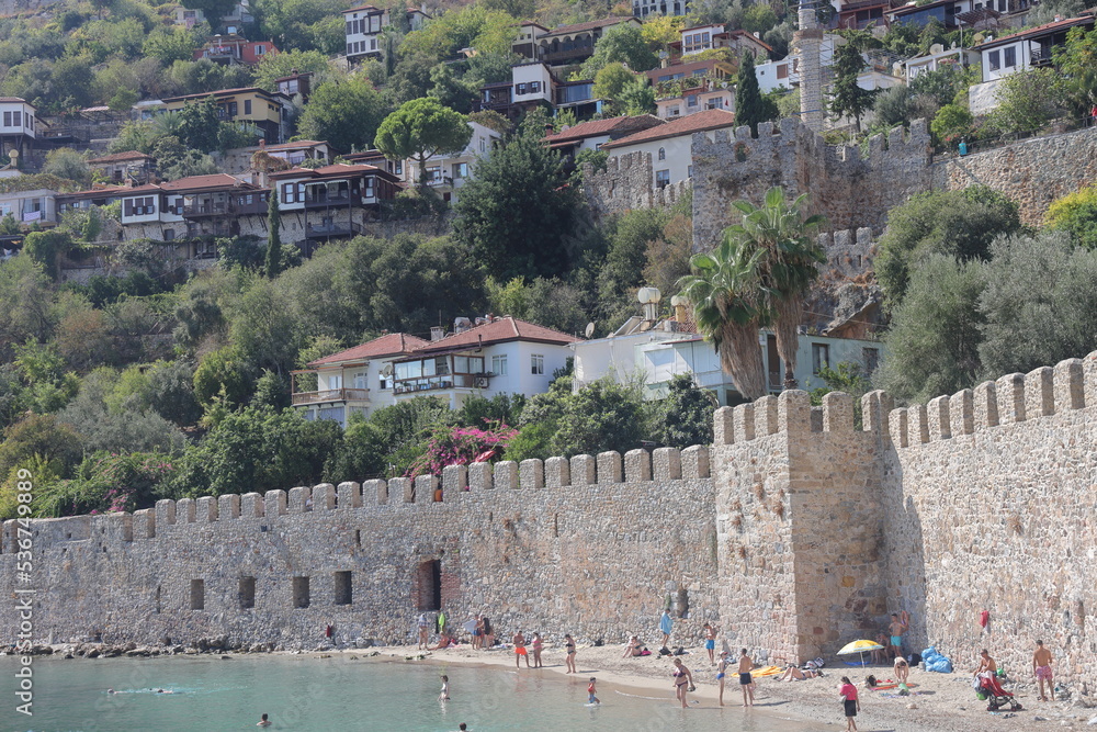 Obraz premium ALANYA, Turkey - October 2022: Alanya city beach near the fortress wall. Urban development on a mountain slope. October 2022. Turkey.