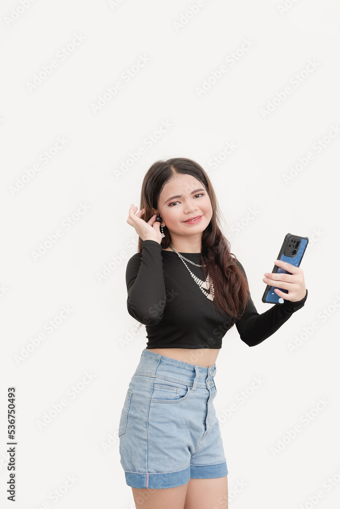 A happy young woman holds her new wireless earbuds and cellphone as she proudly shows the camera for a studio shot isolated on a white background. A happy young woman holds her new wireless earbuds and cellphone as she proudly shows the camera for a studio shot isolated on a white background.