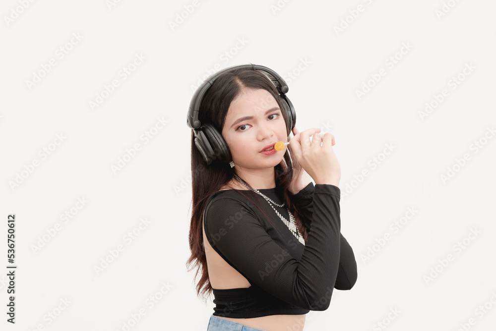A young lady wearing a black wireless headphones holds a lollipop while posing for a studio shot isolated on a white background. A young lady wearing a black wireless headphones holds a lollipop while posing for a studio shot isolated on a white background.
