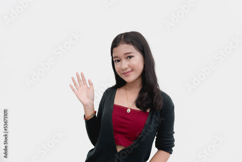 A courteous young lady waves hello to the camera for a studio shot isolated on a white background.