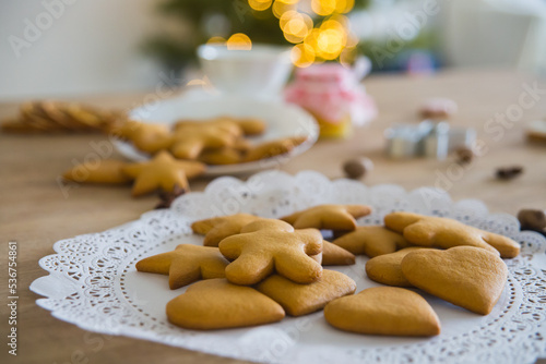 Plate with traditional ginger cookies in front of a Christmas tree with a herald of lights. 