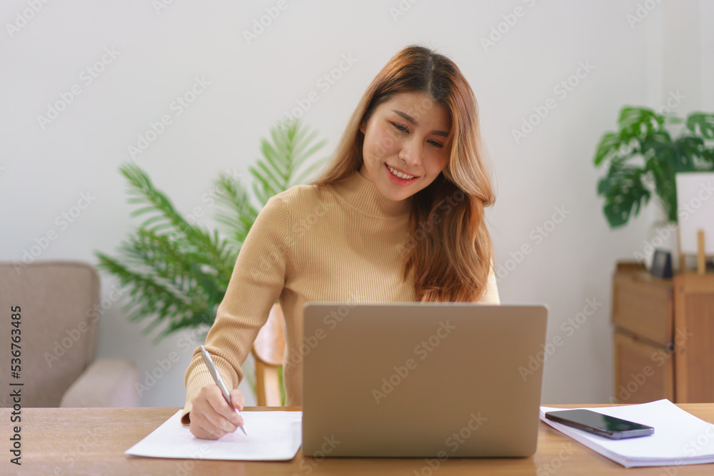 Work from home concept, Young Asian woman reading data on laptop and taking notes on notebook Work from home concept, Young Asian woman reading data on laptop and taking notes on notebook