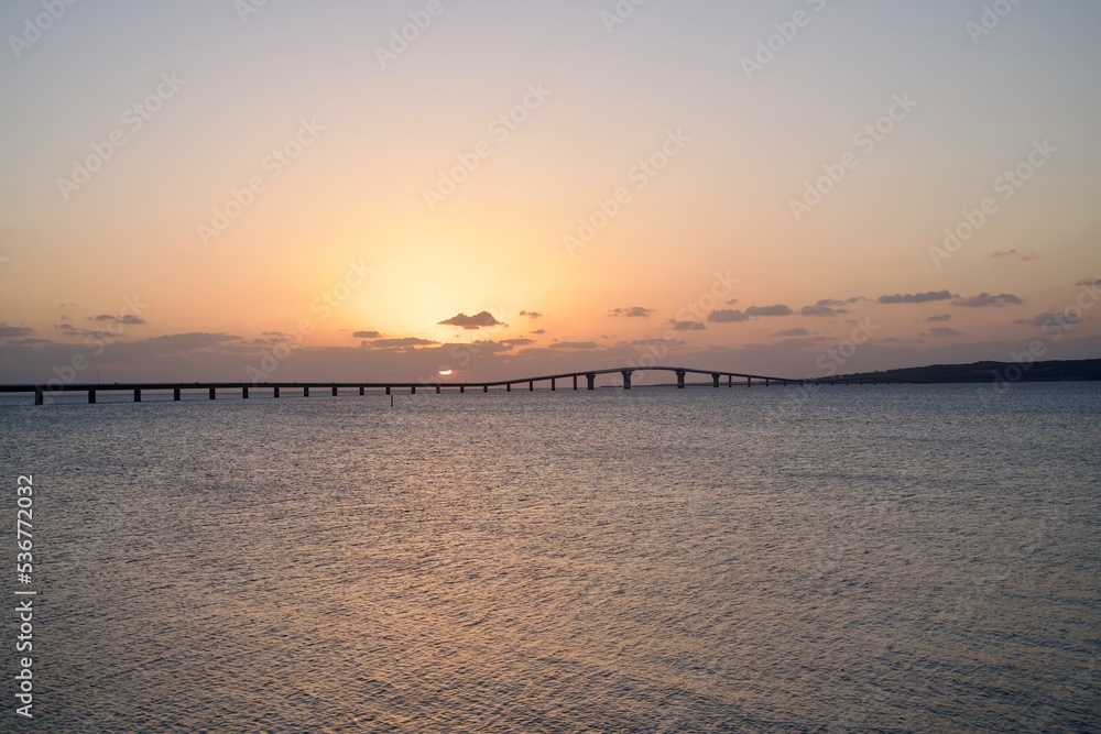 The sunset slightly hidden by clouds and the view of the Irabu Bridge