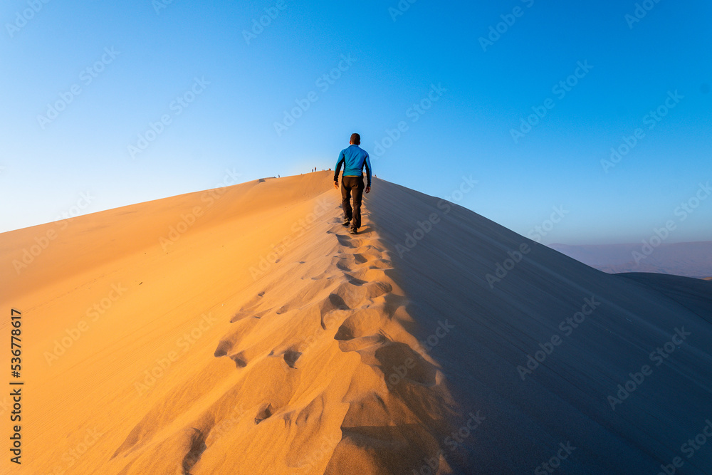 a man is walking throught sand dunes in huacachina, peru