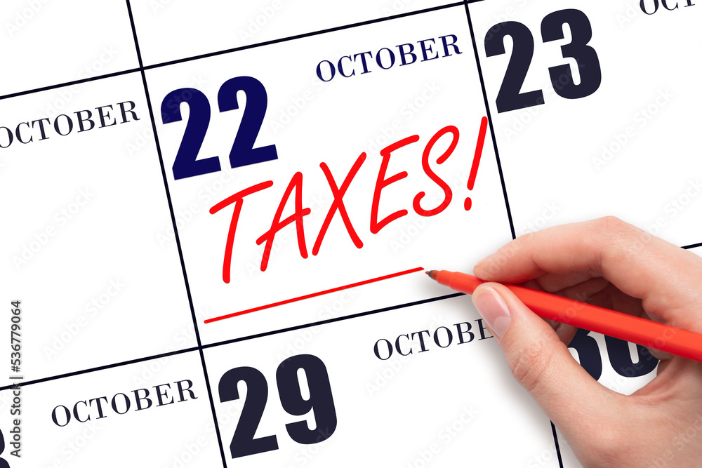 Hand drawing red line and writing the text Taxes on calendar date October 22. Remind date of tax payment Hand drawing red line and writing the text Taxes on calendar date October 22. Remind date of tax payment