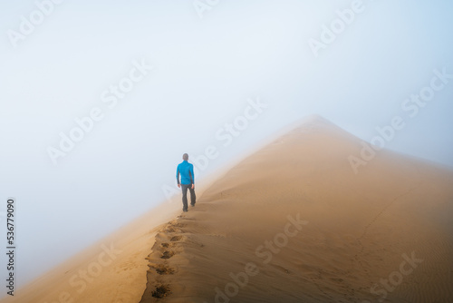 a man is walking throught sand dunes in huacachina  peru