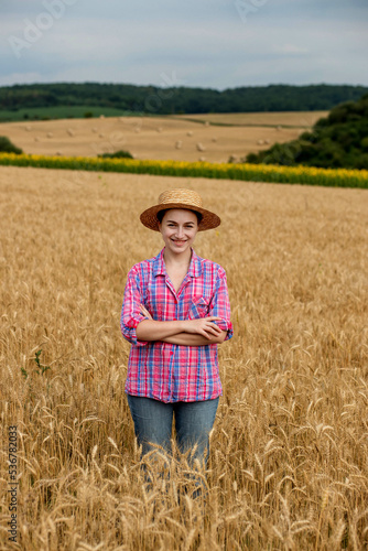 Young farmer woman in straw hat and checkered shirt on wheat ripe golden field. Agriculture. Wheat ripens