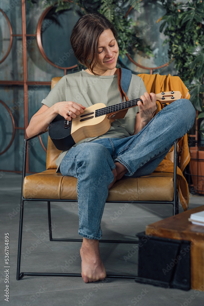 Smiling young woman playing ukulele sitting on the chair