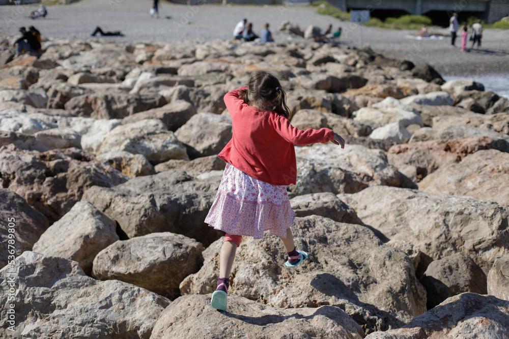 Little girl jumping on rocks on the French riviera during a sunny spring day.