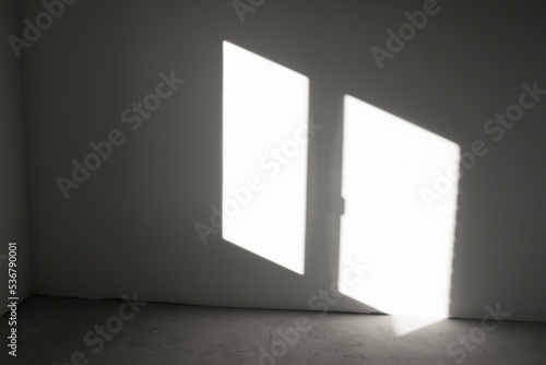 Window-shaped sunlight hitting a dark gray wall inside an empty room. Abstract background with geometric lines.
