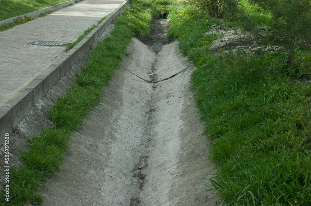 concrete gutter next to the path, green grass all around concrete gutter next to the path, green grass all around