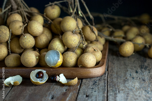 Longan fruit is placed in a wooden rectangle tray and rests on a rustic wooden background.