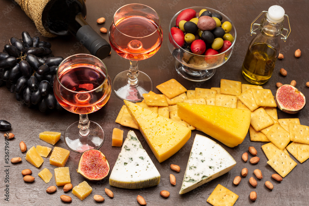 Appetizer set for aperitif. Cheese and crackers, figs and nuts. Bottle of red wine and two glasses of wine.. Colored olives in glass bowl.
