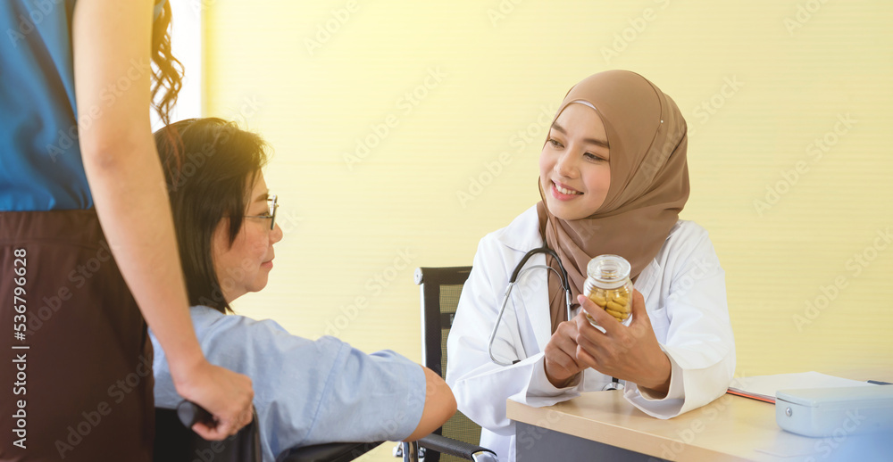 Young asian woman muslim doctor holding the bottle of pills and explaining to elderly patient with her daughter in the hospital office. Young asian woman muslim doctor holding the bottle of pills and explaining to elderly patient with her daughter in the hospital office.