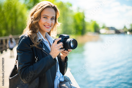 Photos Young smiling woman holding a reflex camera outdoor