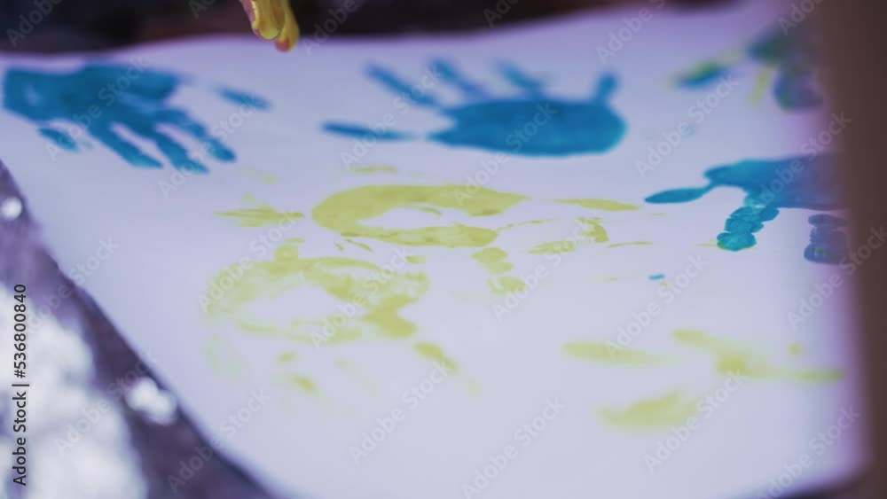 Children's picture on Whatman. Kid have fun and create picture. Children dip hand in paint and apply it to white sheet and palm with fingers is displayed on paper. Blue and yellow colors. Close up Children's picture on Whatman. Kid have fun and create picture. Children dip hand in paint and apply it to white sheet and palm with fingers is displayed on paper. Blue and yellow colors. Close up