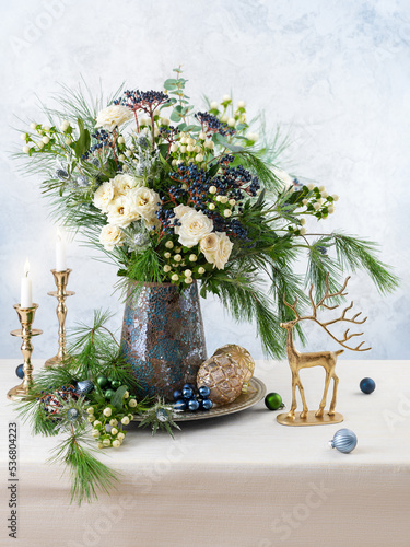 Christmas decorations, candles and flower bouquet. Winter arrangement with roses, fir branches, winter berries. Christmas flower still life. photo