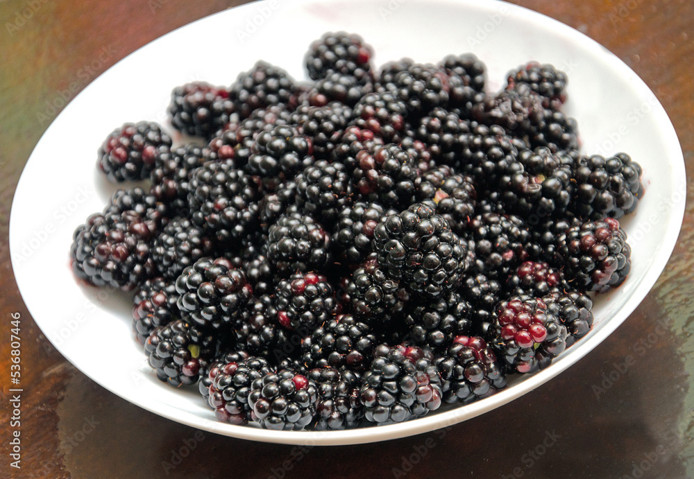 Black juicy blackberries on a white plate on a dark wooden background. blackberry berries top view Black juicy blackberries on a white plate on a dark wooden background. blackberry berries top view